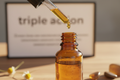 oil dropper dripping essential oil into an amber colored bottle with triple action in the background