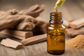 oil dropper dripping essential oils into an amber colored bottle with sandalwood in the background