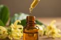 oil dropper dripping in amber colored bottle with ylang ylang in the background