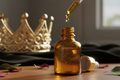 oil dropper dropping essential oil into an amber colored bottle with a crown in the background