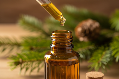oil dropper dropping essential oil into an amber colored bottle with balsam in the background