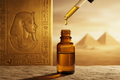 oil dropper dropping essential oil into an amber colored bottle with egyptian images in the background