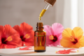 oil dropper dropping essential oil into an amber colored bottle with hibiscus in the background