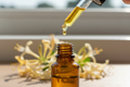 oil dropper dropping essential oil into an amber colored bottle with honeysuckle in the background