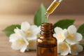 oil dropper dropping essential oil into an amber colored bottle with Jasmine in the background