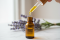 oil dropper dropping essential oil into an amber colored bottle with lavender in the background