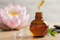 oil dropper dropping essential oil into an amber colored bottle with lotus in the background