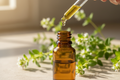 oil dropper dropping essential oil into an amber colored bottle with marjoram in the background