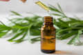 oil dropper dropping essential oil into an amber colored bottle with mugwort in the background
