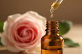 oil dropper dropping essential oil into an amber colored bottle with rose in the background