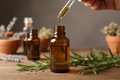 oil dropper dropping essential oil into an amber colored bottle with rosemary in the background