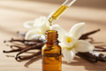 oil dropper dropping essential oil into an amber colored bottle with vanilla in the background