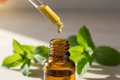 oil dropping dripping essential oil into an amber bottle with spearmint in the background